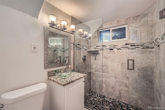 bathroom with a textured wall, toilet, a sink, a shower stall, and a textured ceiling