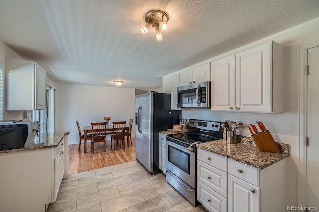 kitchen with a textured ceiling, stainless steel appliances, dark stone countertops, and white cabinets