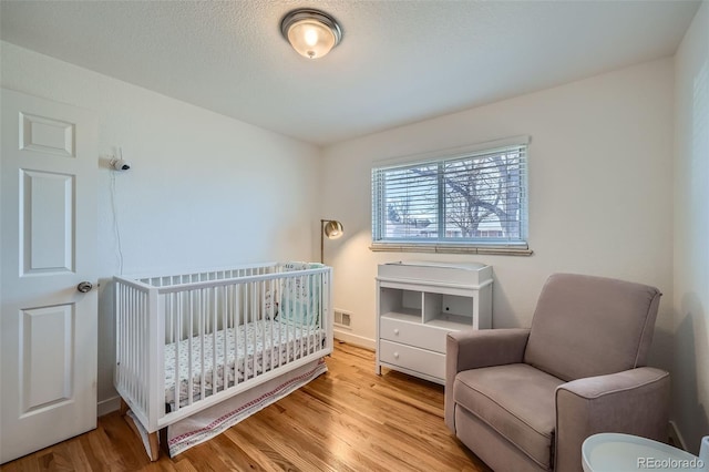 bedroom with a textured ceiling, a crib, wood finished floors, and visible vents