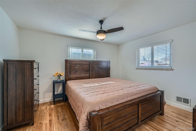 bedroom with baseboards, light wood-style flooring, visible vents, and a textured ceiling