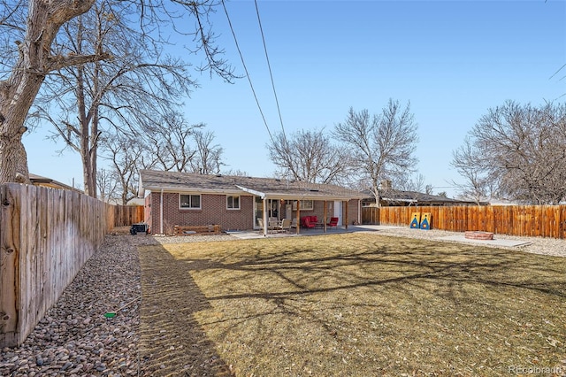 rear view of house with a fire pit, a patio, brick siding, and a fenced backyard