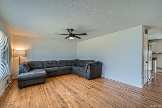 living area featuring light wood finished floors, baseboards, visible vents, a ceiling fan, and a textured ceiling