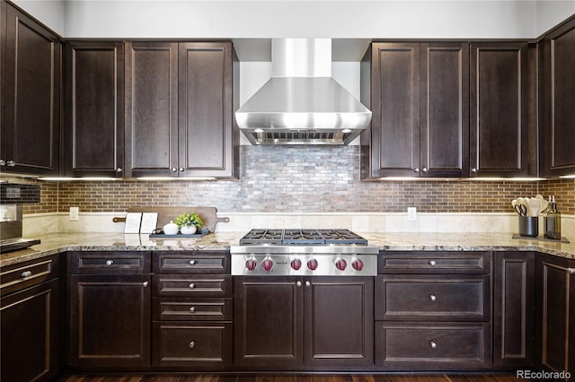 kitchen with backsplash, wall chimney range hood, light stone counters, dark hardwood / wood-style flooring, and stainless steel gas cooktop