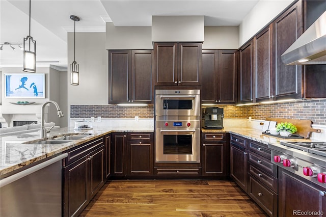 kitchen featuring appliances with stainless steel finishes, wall chimney range hood, sink, decorative light fixtures, and dark hardwood / wood-style floors