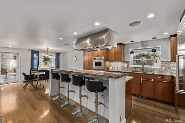 kitchen with sink, oven, island exhaust hood, and pendant lighting