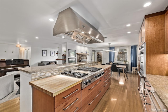 kitchen featuring butcher block counters, island range hood, light hardwood / wood-style floors, a spacious island, and stainless steel gas stovetop