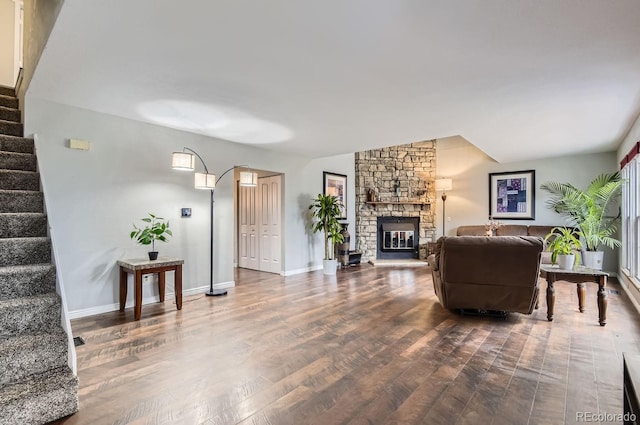 living room with a stone fireplace, wood-type flooring, and vaulted ceiling