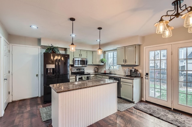 kitchen featuring sink, dark stone countertops, appliances with stainless steel finishes, a kitchen island, and pendant lighting