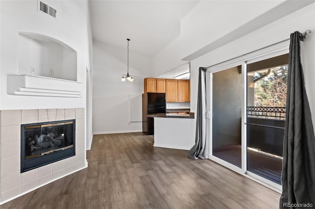 kitchen with black refrigerator, pendant lighting, light brown cabinetry, a tile fireplace, and dark hardwood / wood-style floors