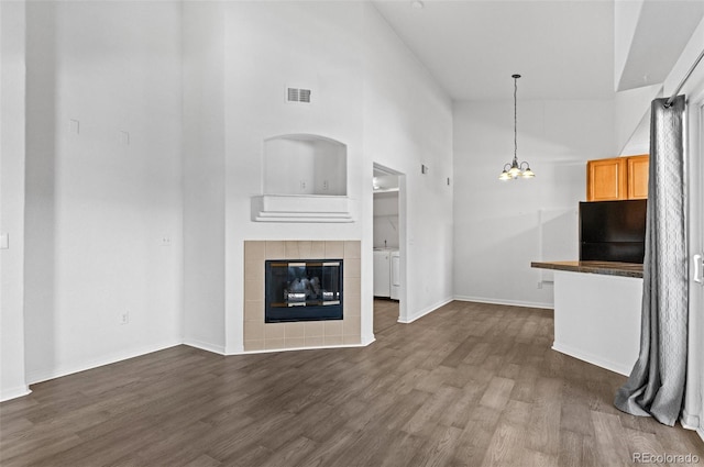 unfurnished living room featuring a tiled fireplace, dark wood-type flooring, a towering ceiling, and an inviting chandelier