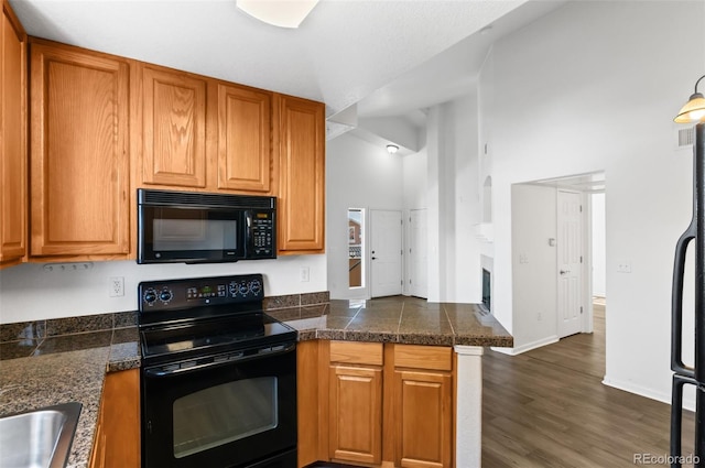 kitchen with black appliances, a towering ceiling, sink, kitchen peninsula, and dark hardwood / wood-style floors