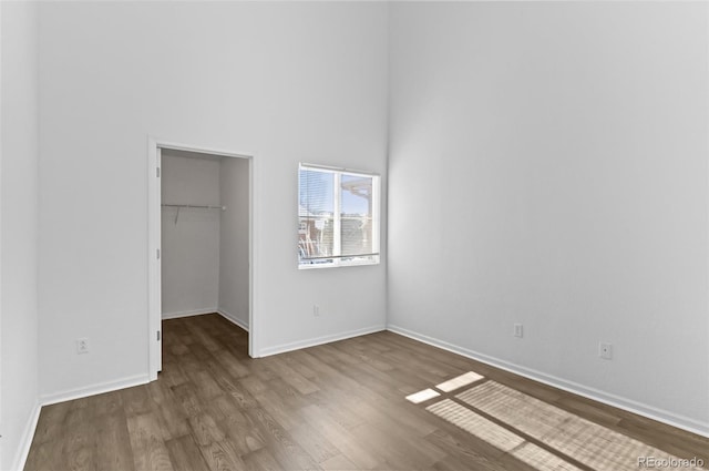 unfurnished bedroom with wood-type flooring, a closet, a high ceiling, and a walk in closet