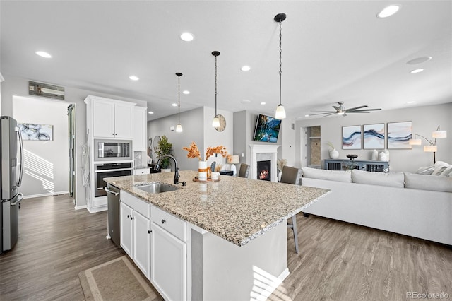 kitchen with stainless steel appliances, a kitchen island with sink, sink, pendant lighting, and white cabinetry