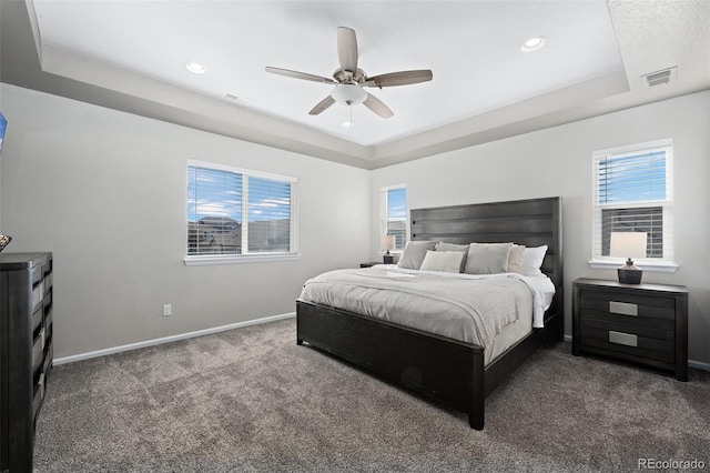 bedroom featuring ceiling fan, dark carpet, and a tray ceiling