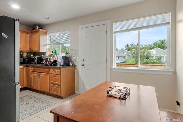 kitchen featuring freestanding refrigerator, brown cabinets, dark countertops, and light tile patterned floors