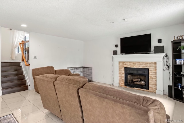 living room featuring a textured ceiling, light tile patterned flooring, a fireplace, baseboards, and stairway