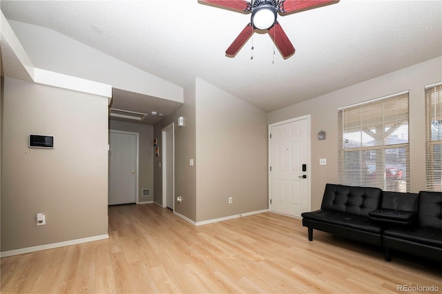 living area with baseboards, light wood-style flooring, a ceiling fan, and vaulted ceiling