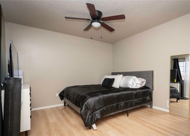 bedroom with ceiling fan, baseboards, light wood-type flooring, and a textured ceiling