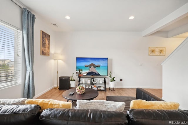 living room with beamed ceiling, light wood-type flooring, and plenty of natural light