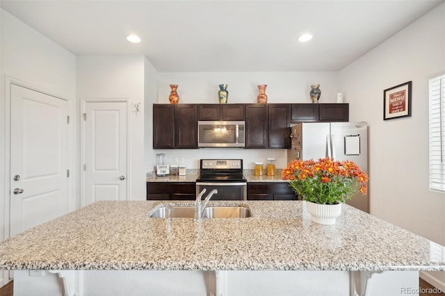 kitchen with light stone countertops, appliances with stainless steel finishes, sink, a kitchen bar, and a center island with sink