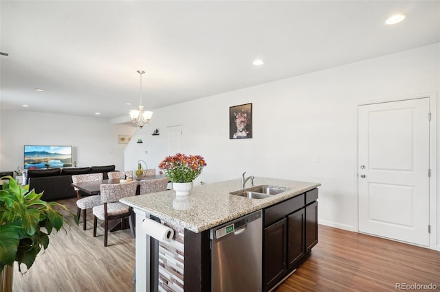 kitchen with sink, dishwasher, light hardwood / wood-style floors, decorative light fixtures, and a kitchen island with sink