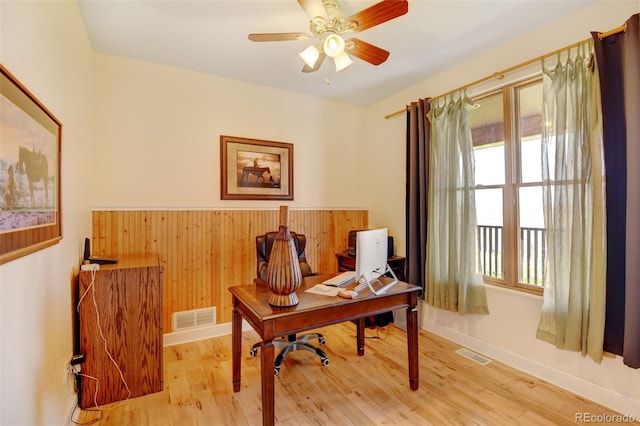 home office featuring wood walls, ceiling fan, and light hardwood / wood-style flooring