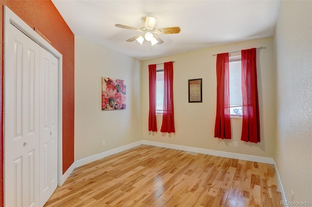 unfurnished bedroom with a closet, light wood-type flooring, multiple windows, and ceiling fan