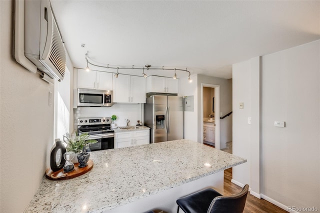 1349 Race St Unit 5, Denver, CO 80206 - kitchen featuring stainless steel appliances, a peninsula, wood finished floors, light stone counters, and white cabinets