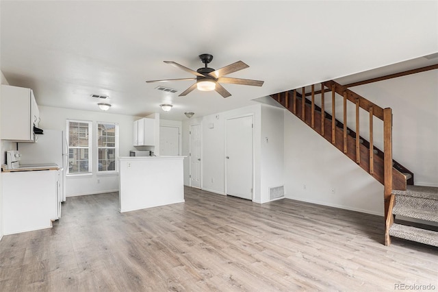 unfurnished living room with ceiling fan, visible vents, light wood-style flooring, and stairway
