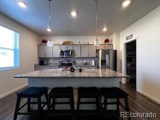 kitchen featuring appliances with stainless steel finishes, a kitchen island with sink, backsplash, and a kitchen bar