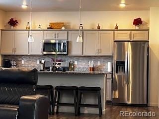 kitchen featuring appliances with stainless steel finishes, dark countertops, a kitchen breakfast bar, and tasteful backsplash