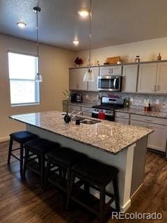 kitchen featuring tasteful backsplash, appliances with stainless steel finishes, a breakfast bar, dark wood-type flooring, and light stone countertops