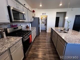 kitchen with decorative backsplash, appliances with stainless steel finishes, a kitchen island with sink, a sink, and light stone countertops