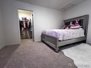 carpeted bedroom with a walk in closet, attic access, and baseboards