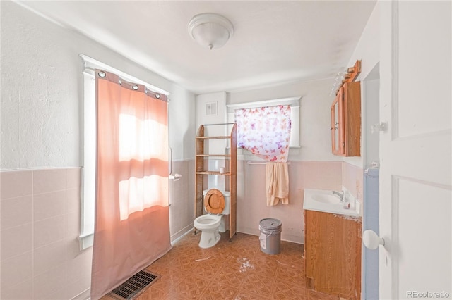 bathroom featuring toilet, visible vents, tile walls, and vanity