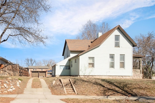 view of home's exterior with roof with shingles, a chimney, and fence