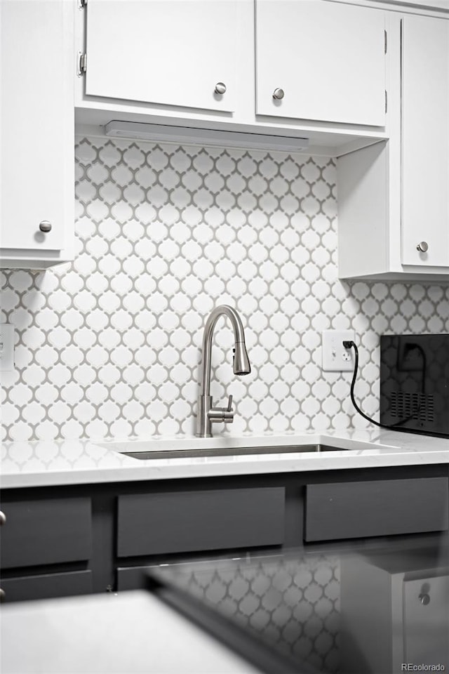 interior details featuring tasteful backsplash, white cabinetry, light countertops, and a sink