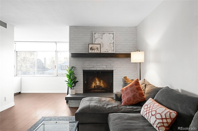 living room with a brick fireplace, baseboards, and wood finished floors