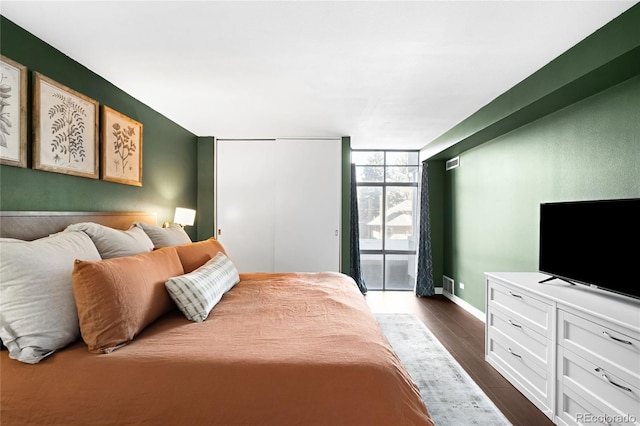 bedroom with access to exterior, a closet, dark wood-type flooring, expansive windows, and baseboards