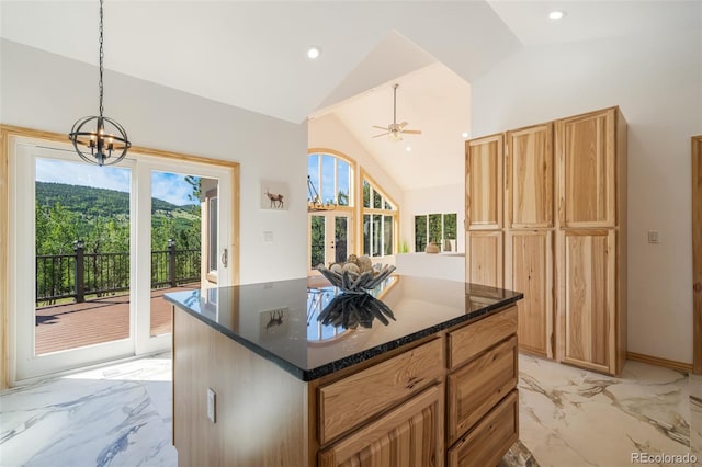 kitchen with hanging light fixtures, high vaulted ceiling, ceiling fan with notable chandelier, a center island, and dark stone counters