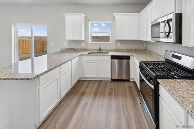 kitchen featuring appliances with stainless steel finishes, light hardwood / wood-style floors, white cabinetry, sink, and light stone counters