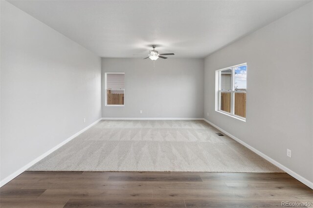 empty room featuring a ceiling fan, baseboards, visible vents, and wood finished floors