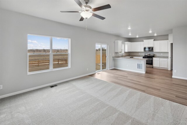 kitchen featuring a peninsula, white cabinetry, open floor plan, appliances with stainless steel finishes, and light stone countertops