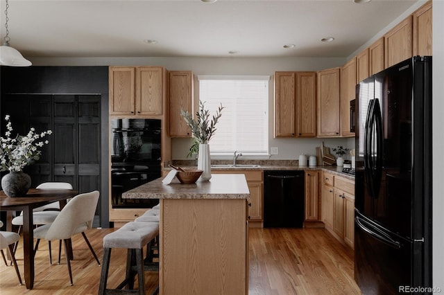 kitchen featuring a kitchen island, a breakfast bar, light wood-style flooring, a sink, and black appliances