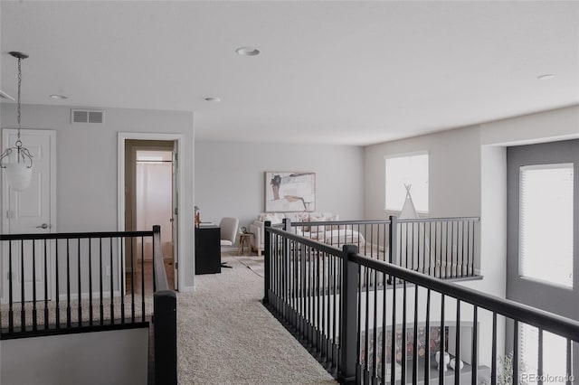 hallway featuring an upstairs landing, visible vents, baseboards, and carpet