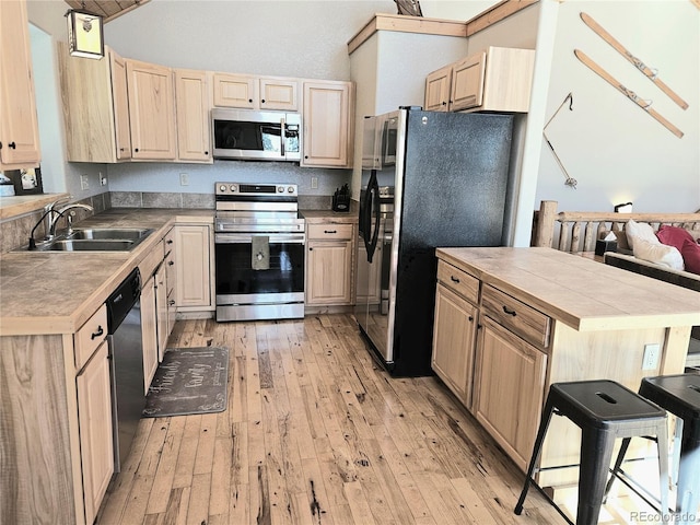 kitchen with light wood-type flooring, light brown cabinets, appliances with stainless steel finishes, and a sink