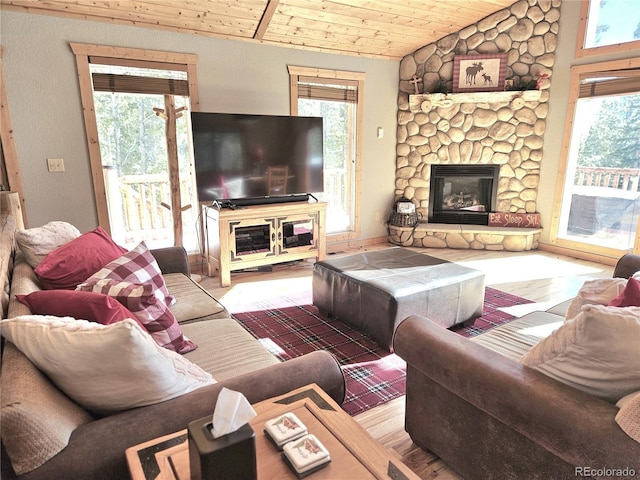 living area with lofted ceiling, wooden ceiling, plenty of natural light, and a stone fireplace