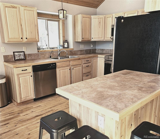 kitchen with light wood finished floors, appliances with stainless steel finishes, light brown cabinets, vaulted ceiling, and a sink