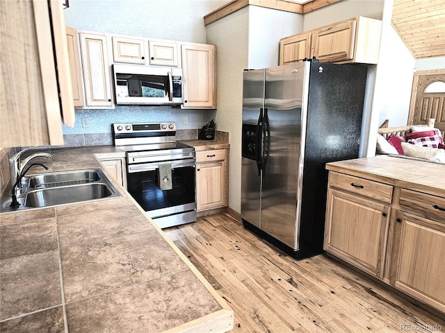 kitchen featuring appliances with stainless steel finishes, a sink, light wood finished floors, and light brown cabinetry