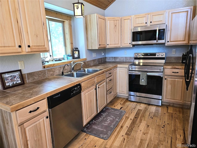 kitchen featuring lofted ceiling, light wood-style flooring, appliances with stainless steel finishes, light brown cabinets, and a sink